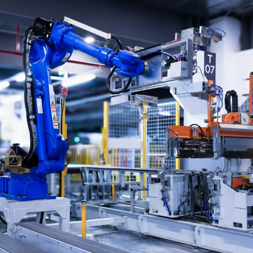 Blue industrial robotic arm operating automated machinery in a modern manufacturing facility with metal components.
