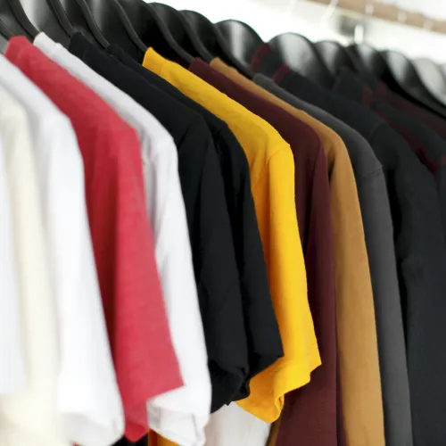 Colorful t-shirts hanging on black hangers in a clothing store rack with white, red, yellow, and black shirts.