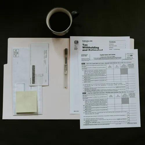 Workspace with tax forms, envelope, pen, and coffee cup on dark surface, organized for filing documents.