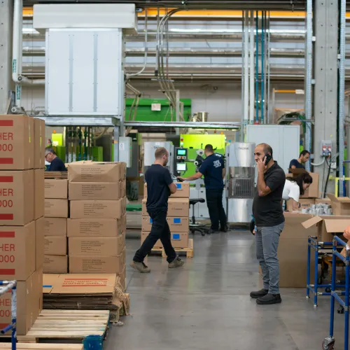 Workers in a factory handling and packing dishwasher boxes with industrial equipment in the background