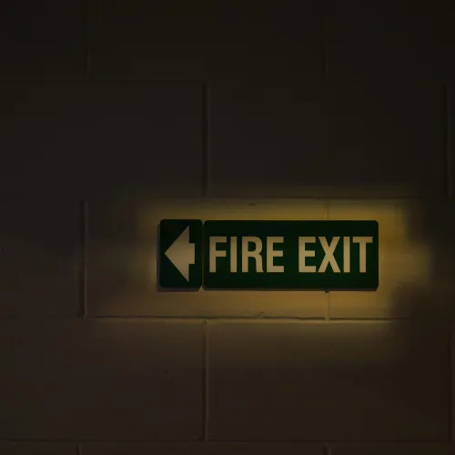 Illuminated green fire exit sign with left arrow on a dark brick wall.
