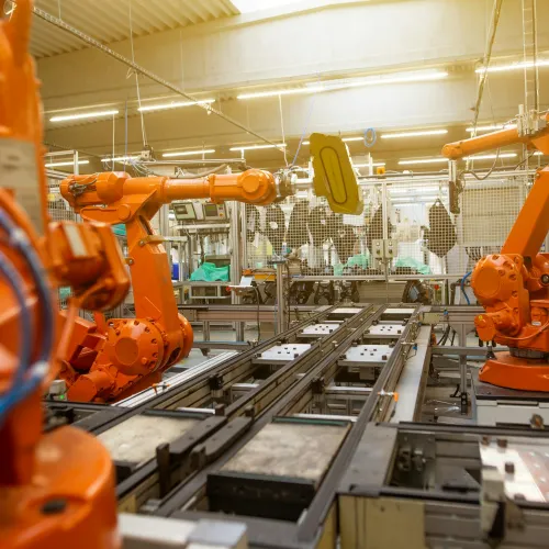 Orange industrial robotic arms working on an automated assembly line in a modern factory setting.