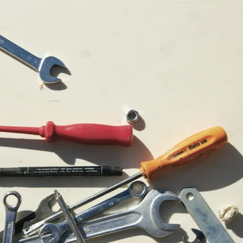 Various hand tools including wrenches, screwdrivers, and a bolt on a light surface with shadows.