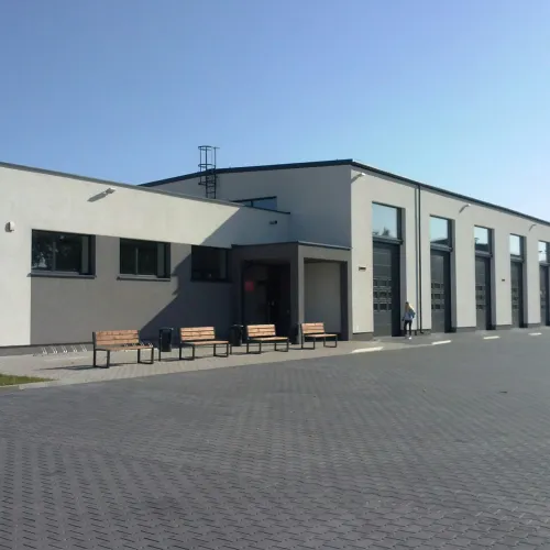 Modern white and gray commercial building with large garage doors and benches in front under clear sky