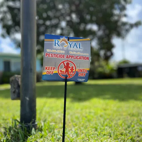 Pesticide application warning sign on a grassy lawn with blurry background of houses and trees.