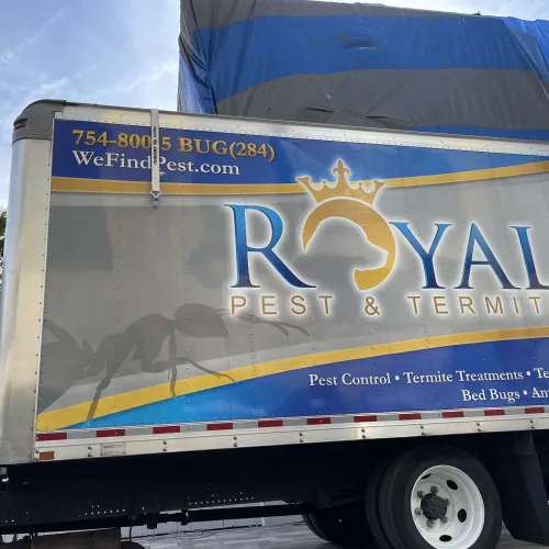 Side of a Royal Pest & Termite truck with logo, contact info, and pest control services listed under a blue sky.