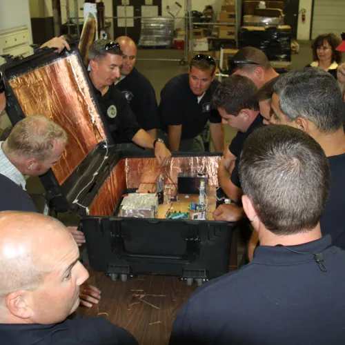 Group of men examining an open black case with electronic components inside in a workshop.
