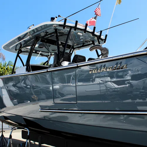 Glossy gray Valhalla boat with flags docked under clear blue sky near palm trees.