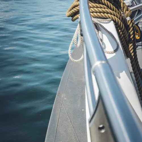 Coiled ropes secured on the railing of a boat with calm blue water in the background under bright daylight.
