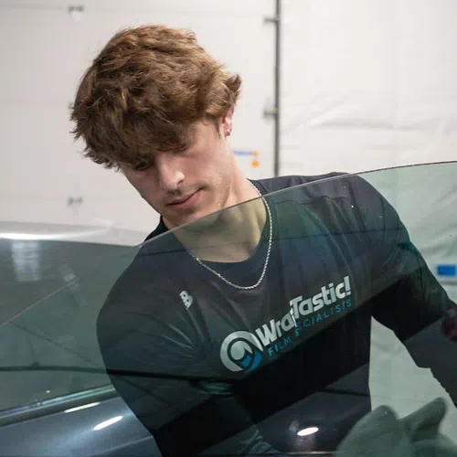 Technician installing or tinting car window glass on a black vehicle in a garage workshop.