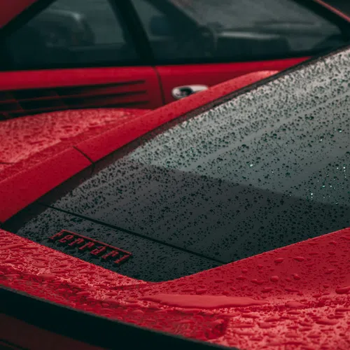 Close-up of red Ferrari cars with rain droplets on the surface highlighting the sleek design and logo.