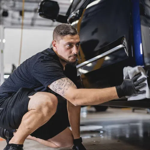 Man cleaning and detailing the side of a black car in a bright automotive workshop.