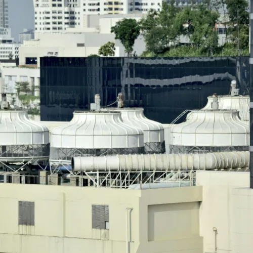 Three large industrial cooling towers on a building rooftop in an urban setting with trees and cityscape in background.