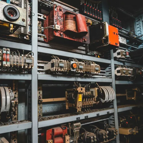 Close-up of old electrical control panel with relays, fuses, wires, and components in industrial setting.