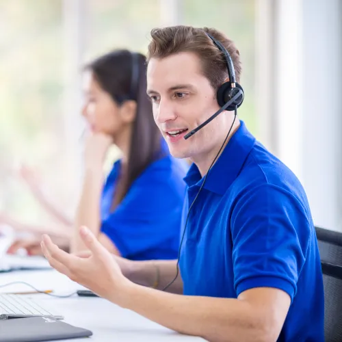 Customer service representatives wearing headsets working at computers in a bright office environment.