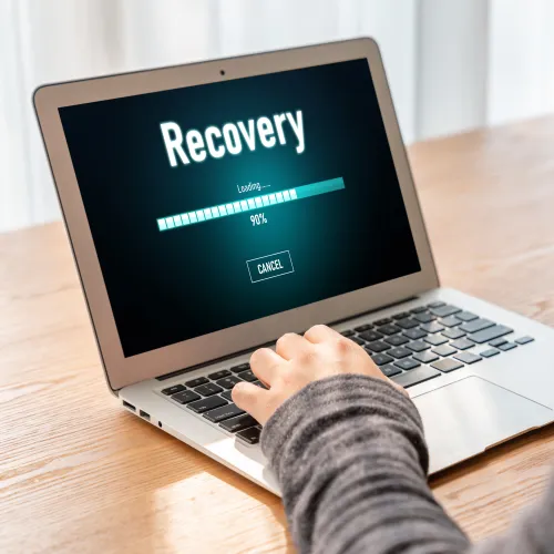 Person using a laptop showing a data recovery progress bar at 90 percent on the screen