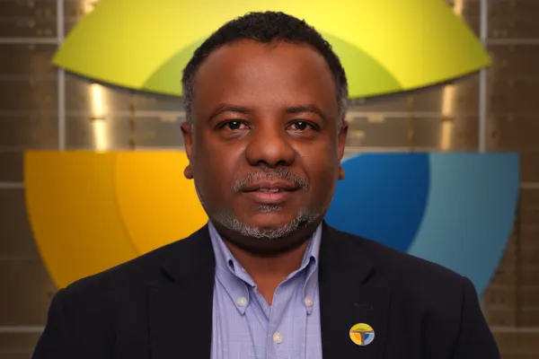 Professional man in suit and blue shirt with colorful modern logo in the background and on his lapel pin.