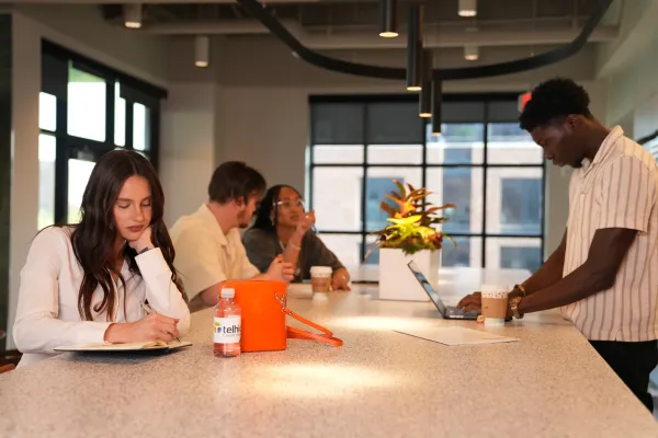 Young professionals collaborating in a modern office with laptops, notebooks, coffee, and casual attire.