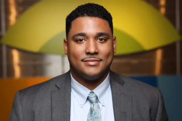 Professional young man in gray suit and patterned tie smiling with colorful blurred background