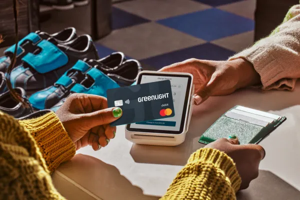 Person using a Greenlight debit card for contactless payment at a point of sale terminal.