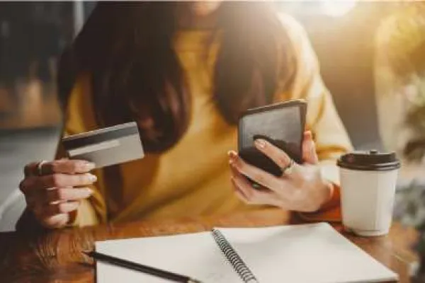 woman in café making purchase with credit card on cell phone