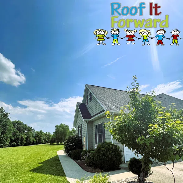 Suburban house with new roof under bright blue sky and Roof It Forward logo with children cartoon above.