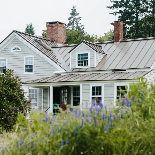 Charming gray house with metal roof surrounded by greenery and flowers in a serene outdoor setting.