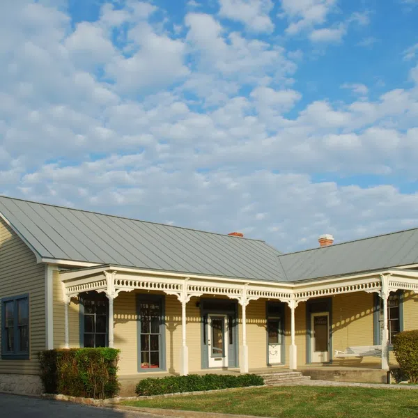 Charming yellow house with a metal roof, surrounded by greenery under a blue sky with fluffy clouds.
