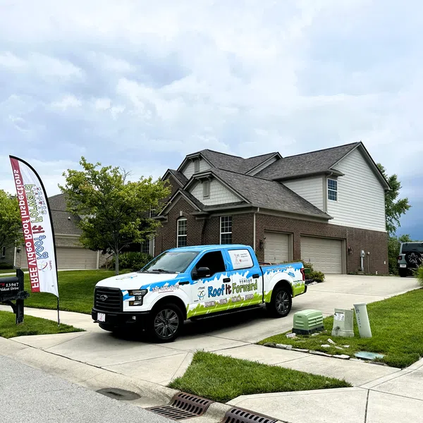 A branded truck parked in front of a suburban home with well-maintained landscaping and cloudy skies.