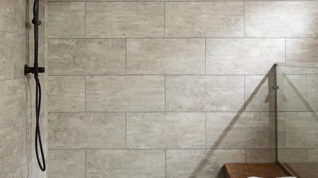 Modern bathroom shower with black rain showerhead, gray tile walls, wooden bench, and folded white towels