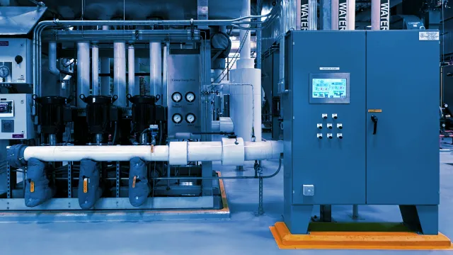 Industrial mechanical room with control panel, pipes labeled feed water, and monitoring gauges for system operation.
