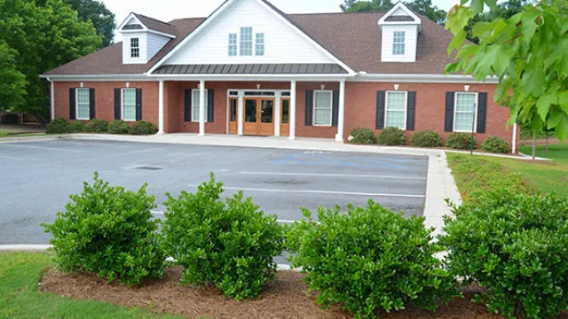 A modern brick building with a manicured lawn and parking area, surrounded by greenery.