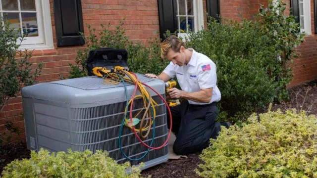 Technician kneeling by an outdoor HVAC unit with tools and hoses, working on air conditioning maintenance.