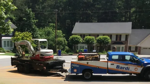 Blue Bardi service truck towing trailer with mini excavator parked in suburban neighborhood drive