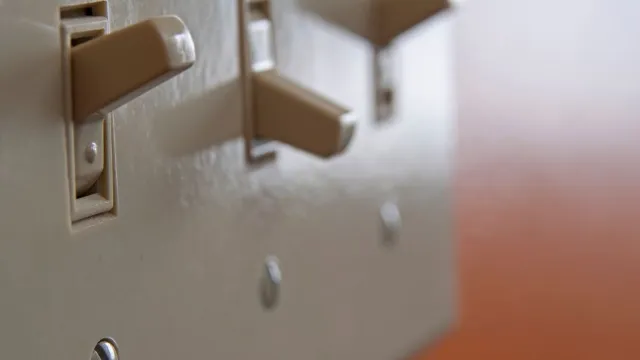 Close-up of three beige light switches on a wall with one switch in the on position and two off.