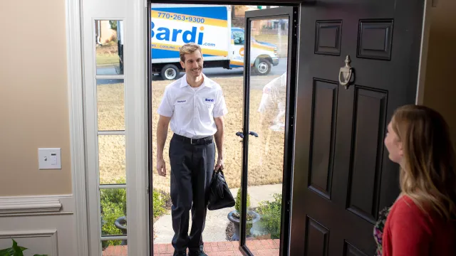 A service technician stands at the door, ready to assist, with a service van visible in the background.