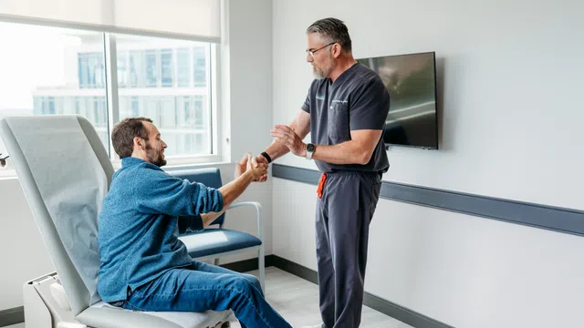 Doctor assisting male patient with arm exercise in a modern medical clinic room with large window.