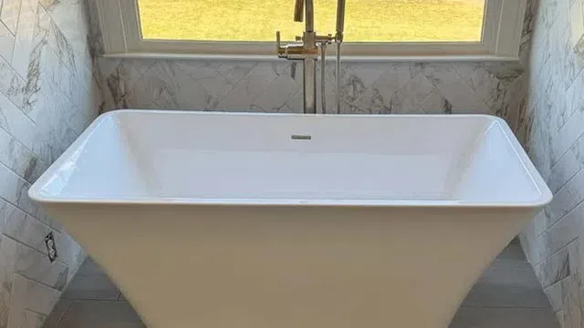 White freestanding bathtub with modern faucet under a large window overlooking a grassy yard.