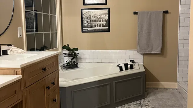 Modern bathroom with patterned tile floor, corner bathtub, wooden vanity, and travel-themed black and white wall art.