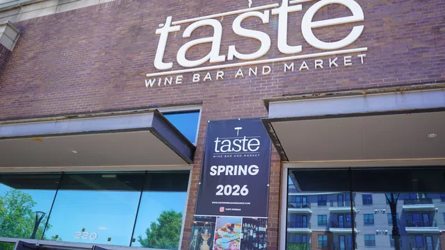 Taste Wine Bar and Market storefront with a Spring 2026 event banner on a brick building under blue sky.