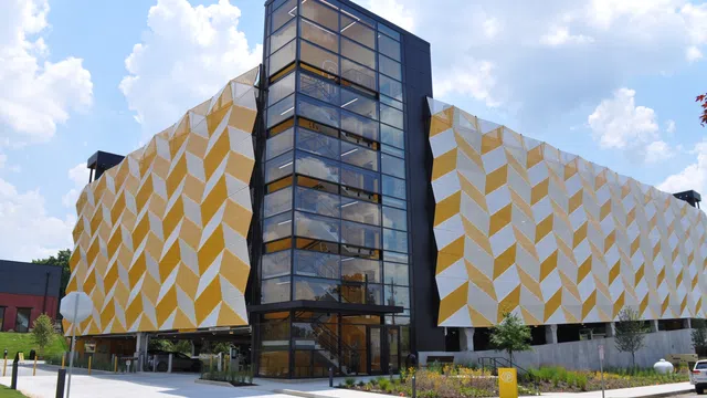 Modern parking garage with geometric yellow and white exterior panels and glass elevator shaft under a blue sky.
