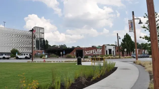 Scofflaw Brewing Co building with green lawn, plants, curved sidewalk, and partly cloudy blue sky