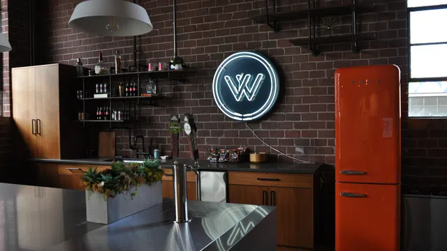 Industrial style kitchen with brick walls, neon sign, orange retro fridge, wooden cabinets, and modern stainless steel island.