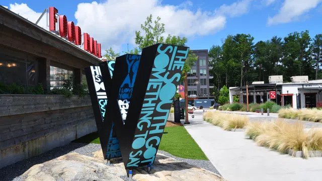 Large decorative 'W' sculpture with text in an outdoor urban park area under blue sky.