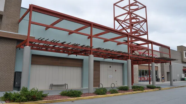 Empty storefront with modern red metal awning structure and overcast sky in a shopping center parking lot