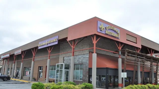 Corner view of a shopping plaza with Louisiana Bistreaux restaurant and various stores under a cloudy sky.