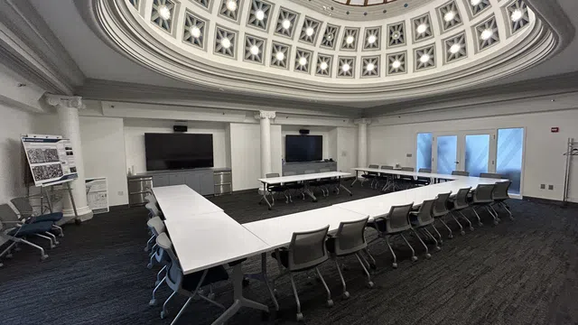 Modern conference room with U-shaped white tables, rolling chairs, and a decorative domed ceiling with lights.