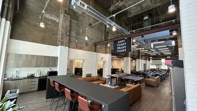 Spacious industrial-style office with high ceilings, lounge areas, kitchen, and multiple seating options under exposed ductwork.