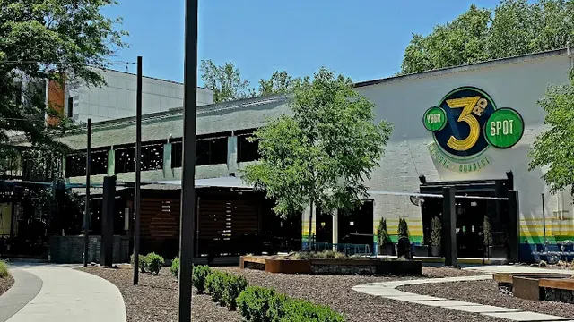 Outdoor view of a rustic restaurant with trees, benches, and a clear blue sky on a sunny day.
