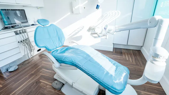 Modern dental clinic with a blue dental chair, equipment, and wooden flooring in a bright room